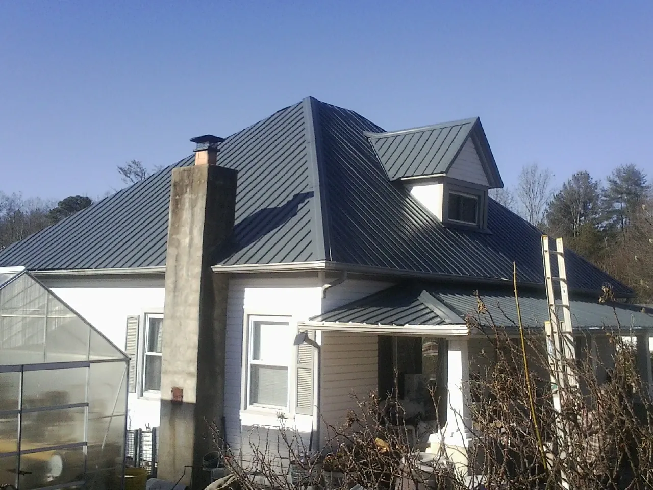 Dark blue standing seam metal roof on a white farmhouse with dormer — Slate & Tile Roof Repair by Roofing Brothers in North Brookfield