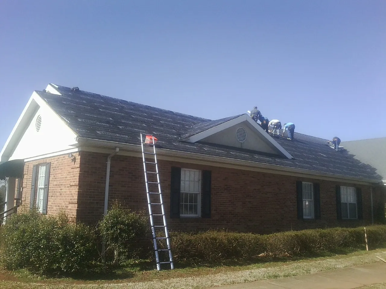 Crew tearing shingles off a brick ranch roof with a ladder set — Emergency Roof Repair work by our crew in North Brookfield