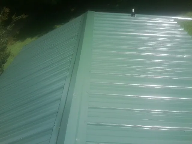 New green metal panels meeting at the ridge of a roof — Flat Roof Repair work by our crew in North Brookfield